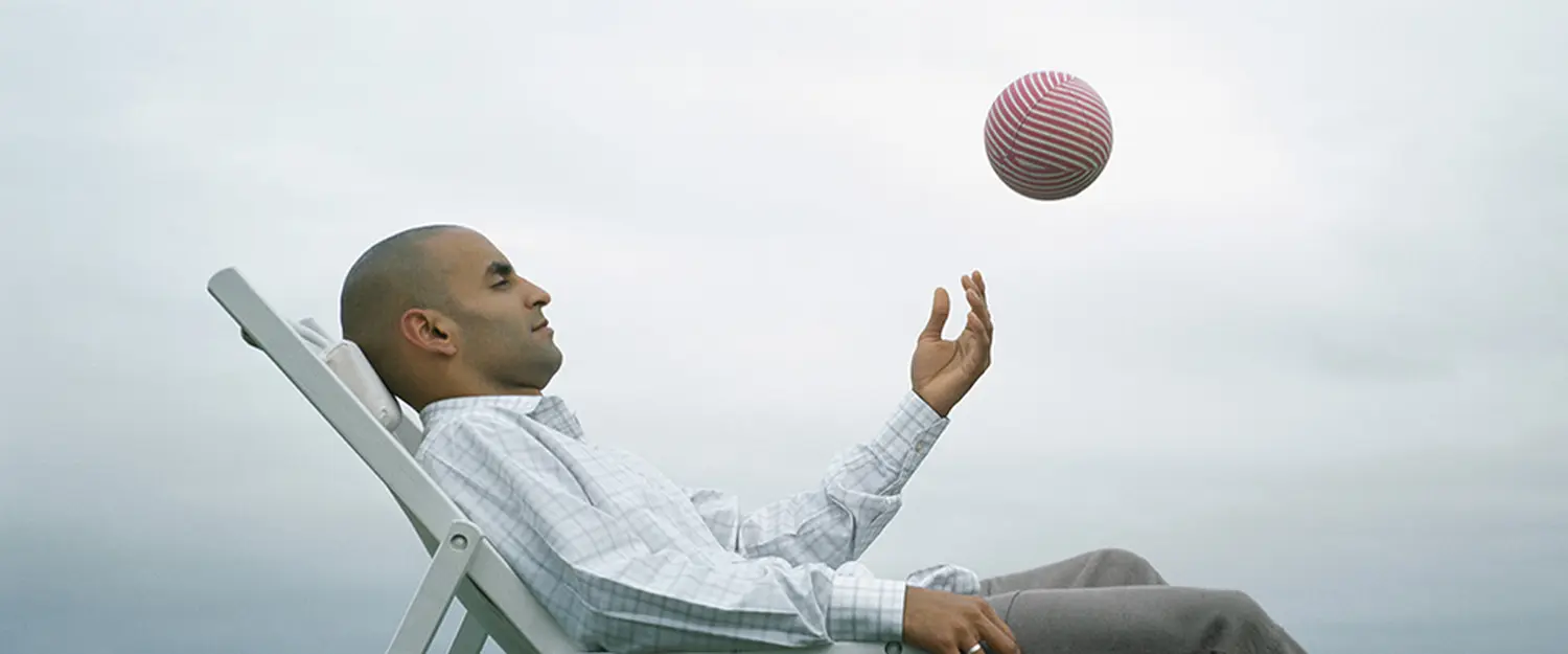 Mann sitzt auf einer Couch und wirft einen Ball